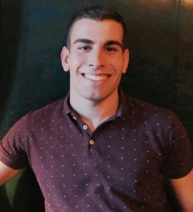 Panos Fragkos PCCh headshot photo, smiling man with dark polo in front of dark background