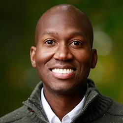 Andrew Dormus PCC headshot photo, smiling man wearing a gray sweater and white collared shirt in front of a green background