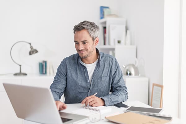 man working in an office at a white desk with his laptop and notebook
