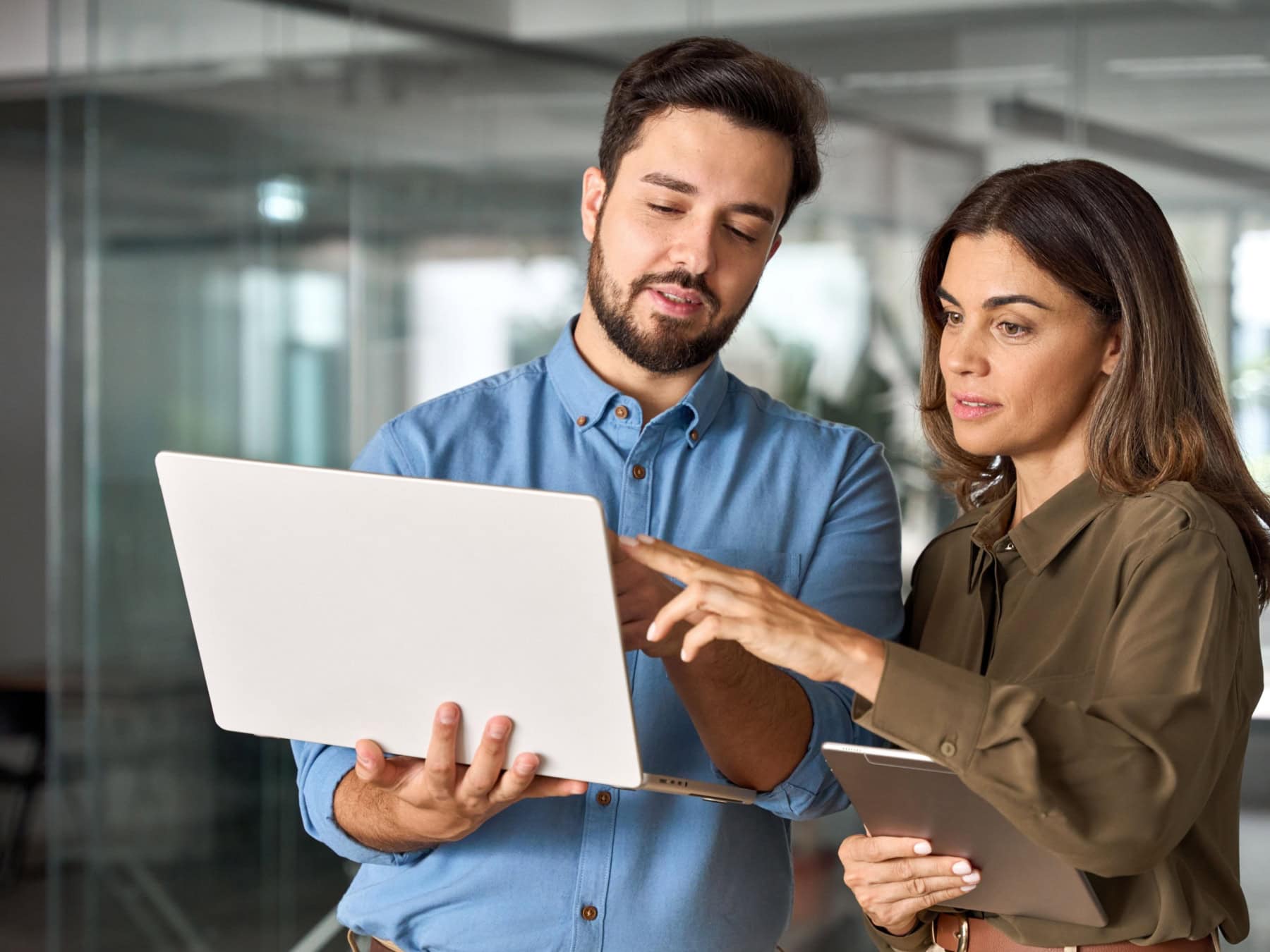 A man and woman compare notes on their computer and tablet in an office.