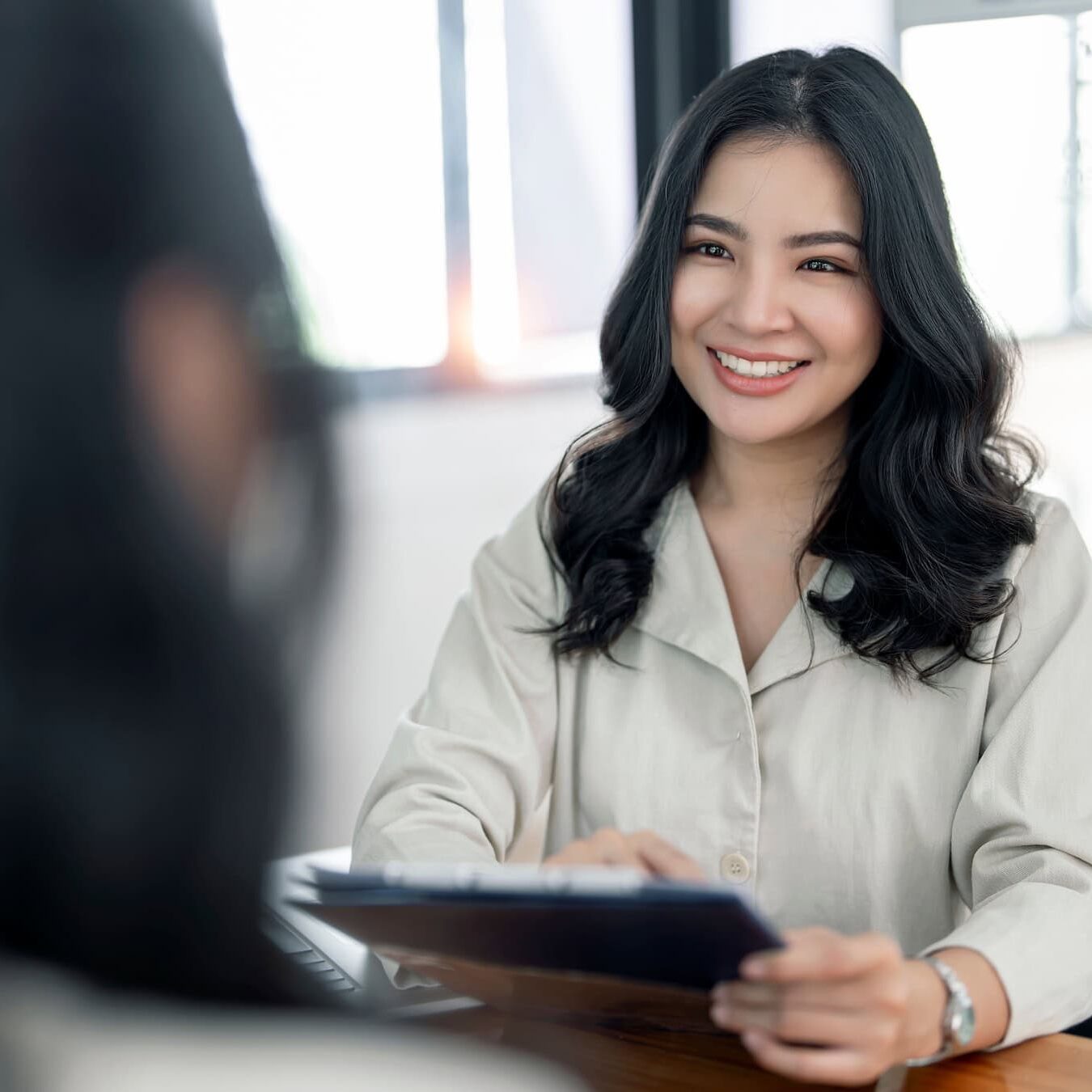 A woman with a tablet is talking to another woman in an office setting