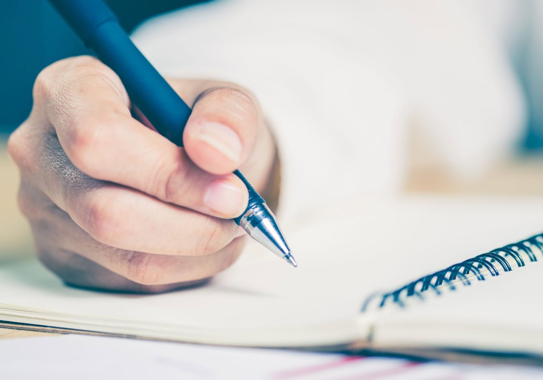 Someone is writing notes in a notebook on a table.