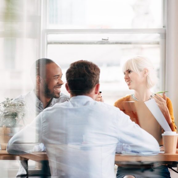 Group of diverse professionals smiling and engaging in a collaborative professional coaching meeting around a table in a bright office.