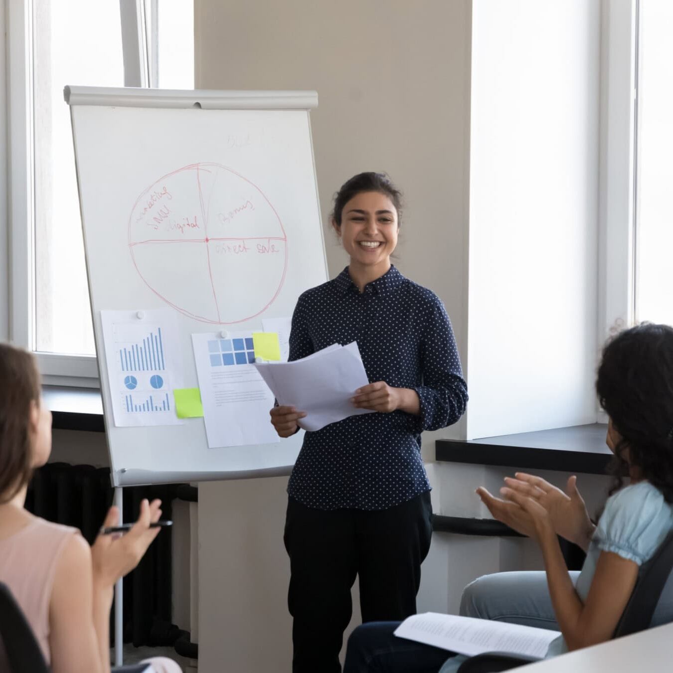 A woman is giving a presentation to a group of people in a casual office.