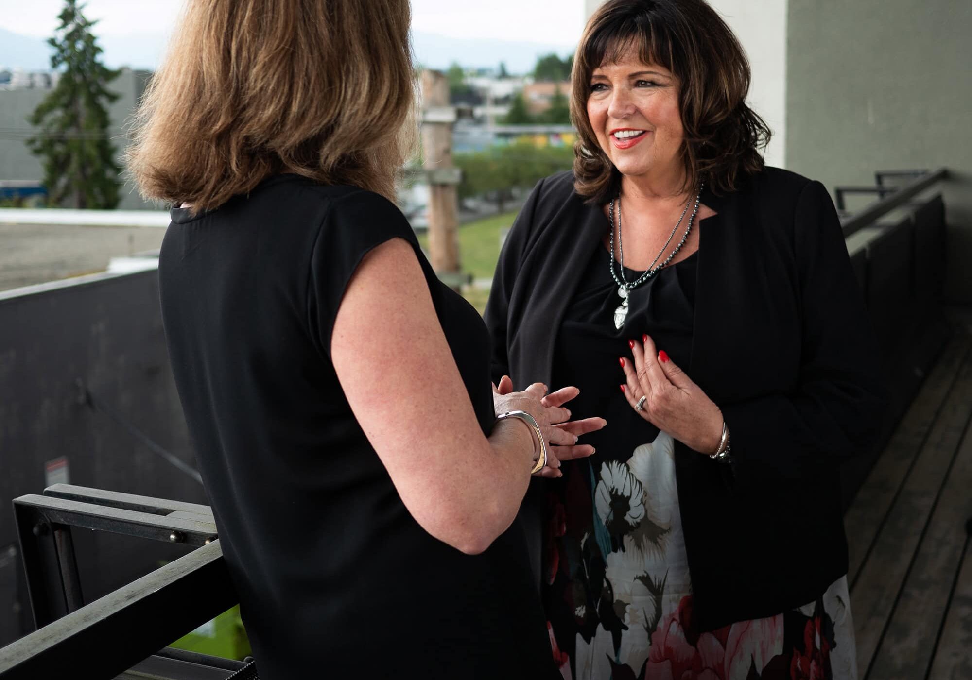 Two women having a professional coaching discussion on a balcony, emphasizing personal and career development.