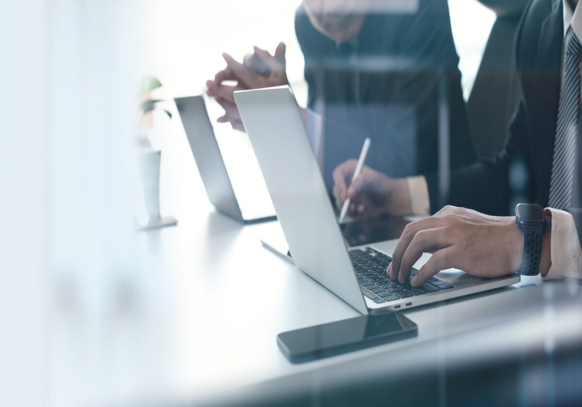 Close-up of business people collaborating in an office, with one person typing on a laptop and another using a stylus on a tablet.