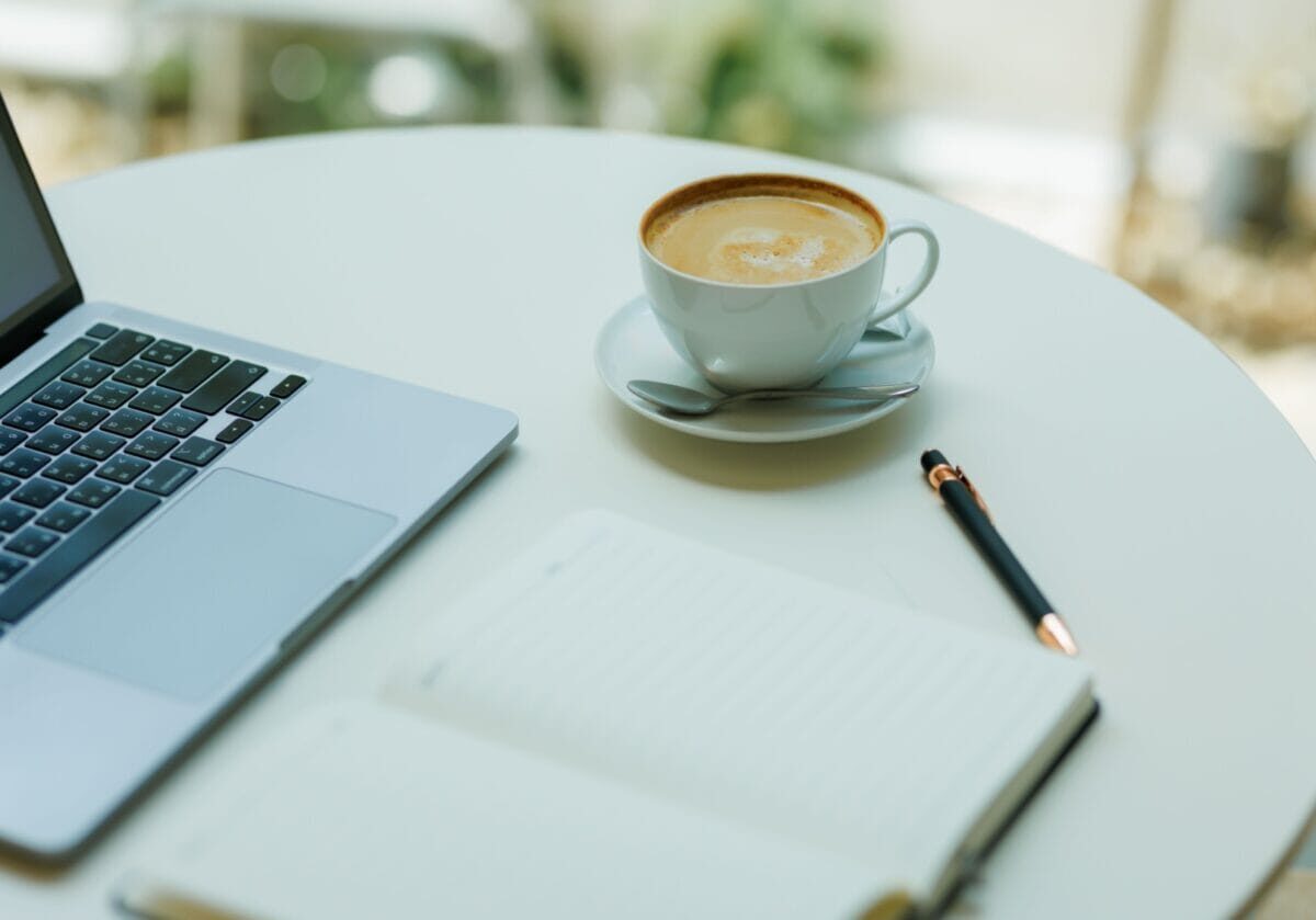 Laptop, notebook, pen, and cup of coffee on a table.