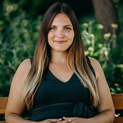 Kalyna Miletic PCC headshot photo, woman with long hair brown to blonde wearing a black top sitting on a park bench