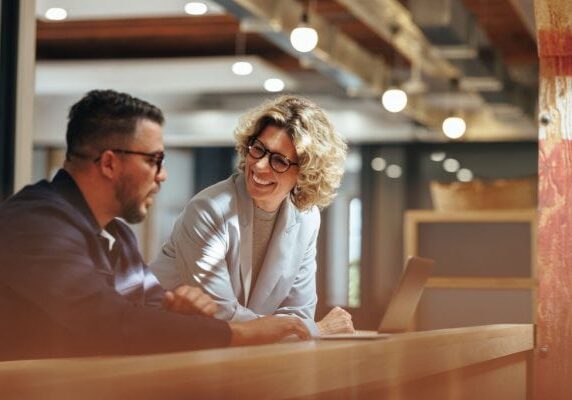 man and woman meeting and looking at a laptop with the woman smiling