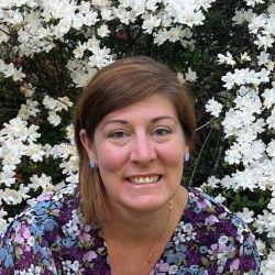 Meredith Pratt headshot photo, dark haired woman sitting with white flowers behind her
