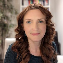 Olga Reinholdt PCC headshot photo, woman with long curled reddish brown hair smiling blurred office background