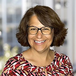 Sandy Stansfield headshot photo, smiling woman with brown hair wearing glasses and red patterned top in front of blurred window