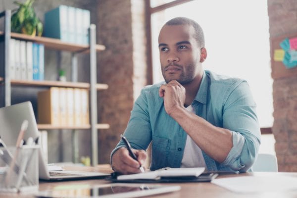 man looking curious and contemplative while writing in a notebook