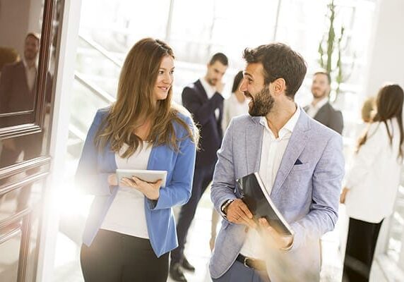 two professionals engaging in conversation and walking in a busy hall way