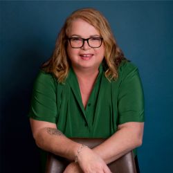 Helen Zink ACTC PCC headshot photo, woman with blond hair green top and glasses smiling blue background