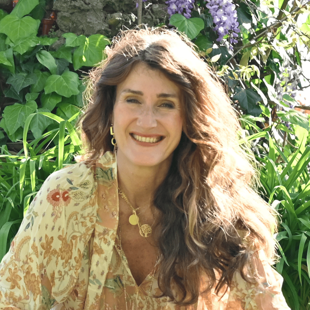 Diana Tedoldi is an Italian leadership and executive coach, she is wearing a white based dressed with orange and red flowers and has a green background.